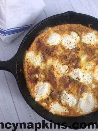This image shows a frittata filled with onion, sweet potato, prosciutto and ricotta that has been baked in a cast iron pan.